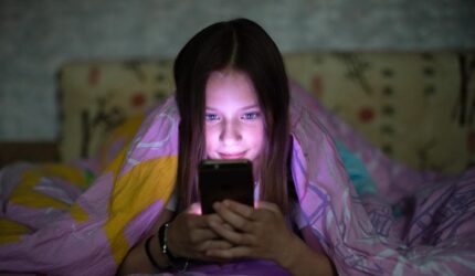 Gadis remaja di bawah selimut menjelajahi telepon