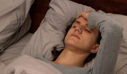 Wanita muda yang lelah melelahkan berbaring di tempat tidur memegangi kepalanya