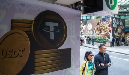 Large Tether (USDT) cryptocurrency signage on a city street in Hong Kong, with pedestrians and storefronts in the background.
